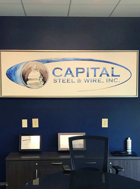Office with large watercolor painting of Capital Steel and Wire logo, framed and hanging on a blue wall.