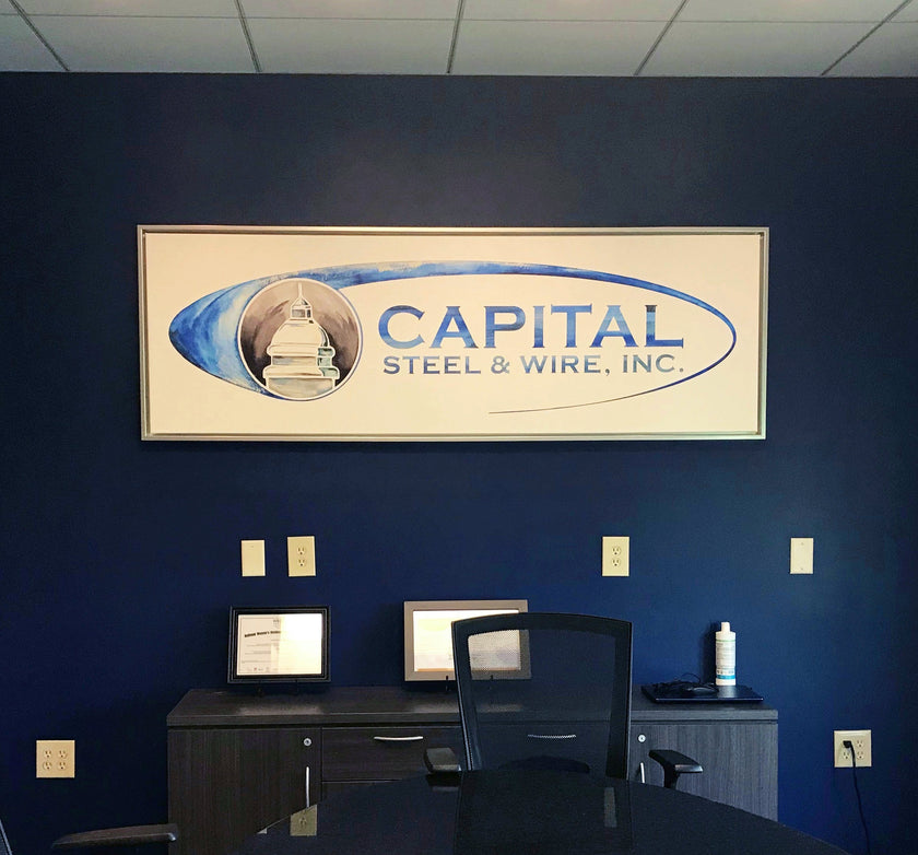 Office with large watercolor painting of Capital Steel and Wire logo, framed and hanging on a blue wall.