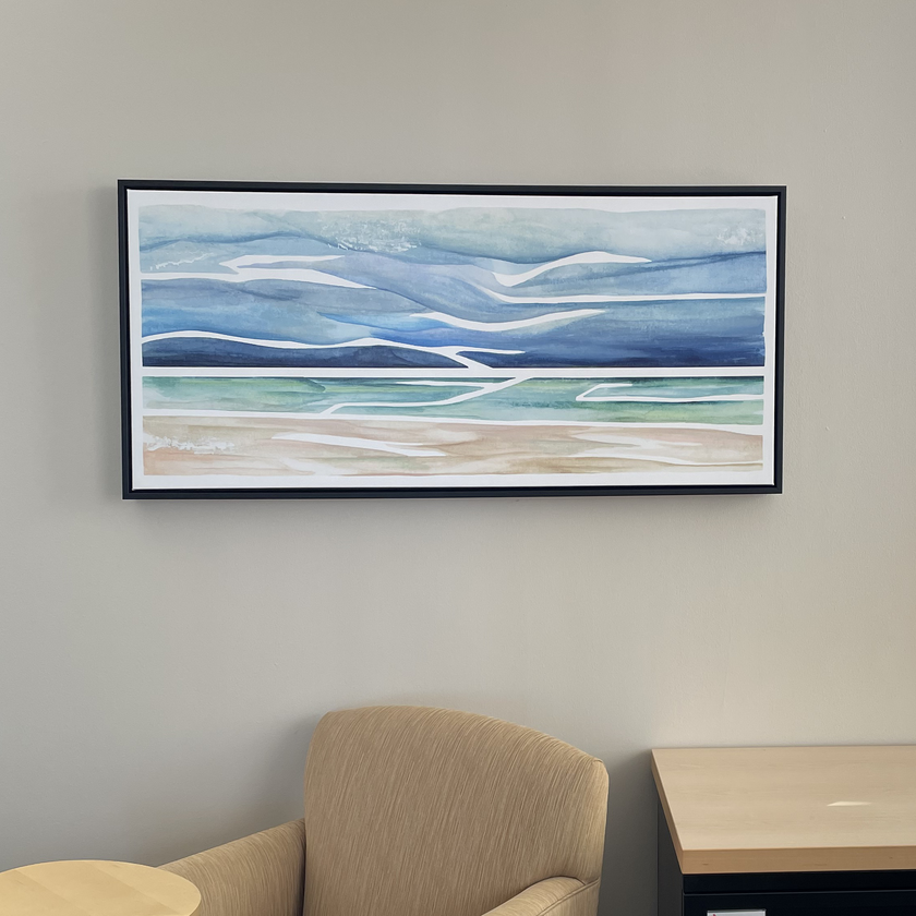 Framed watercolor painting of a beach and lake with stormy sky, hanging in an office.