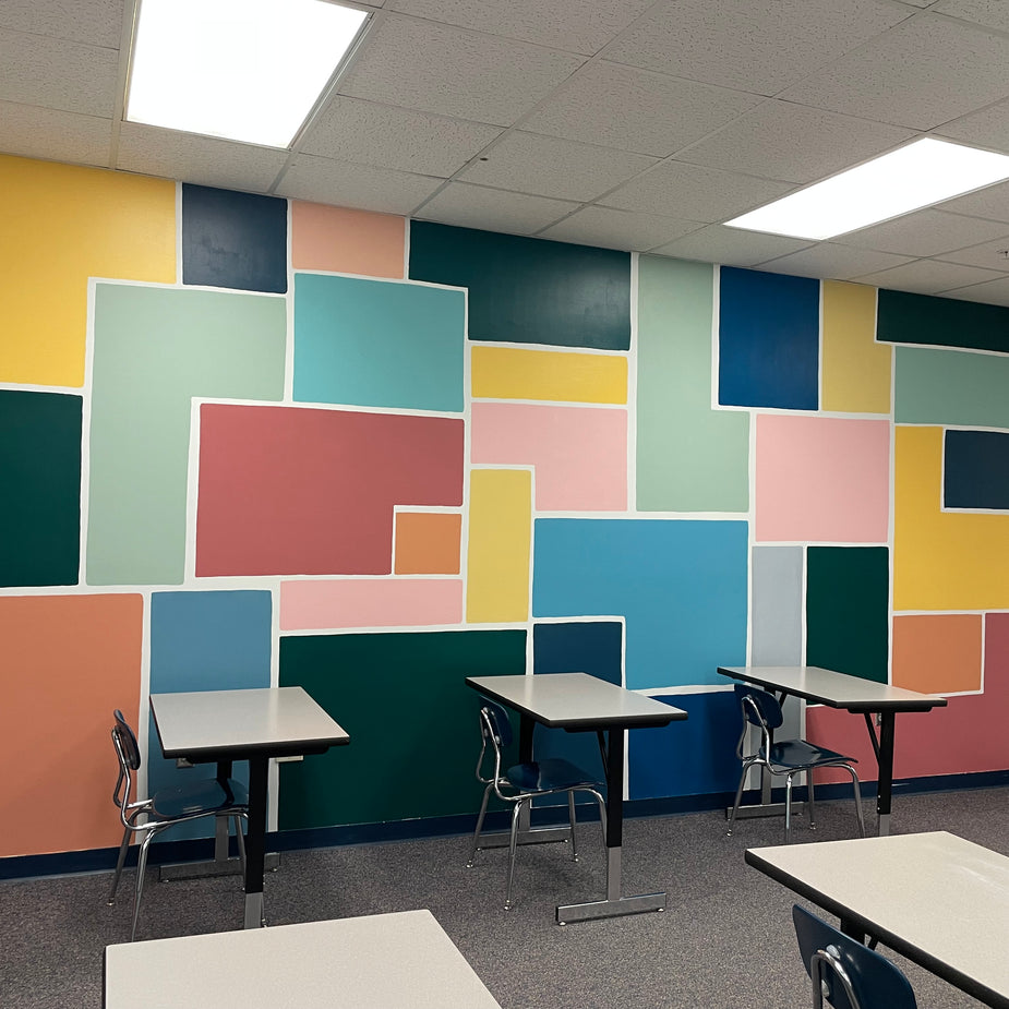 Colorful and bold geometric wall mural in a school classroom with tables and chairs.