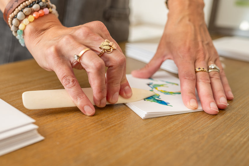 Close-up of artist Emily Frushour's hands as she folds notecards with a bone folder.