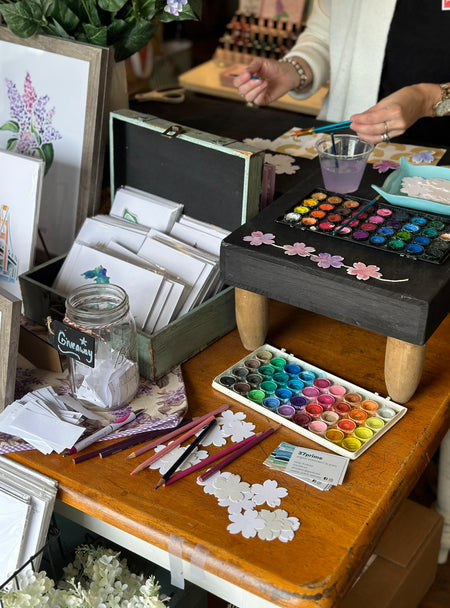 Table with art supplies including watercolor paint, pencils and paper, during an art event with Emily Frushour.