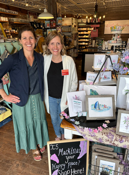 Artist Emily Frushour visiting a gift shop on Mackinac Island and showing watercolor art with store owner.