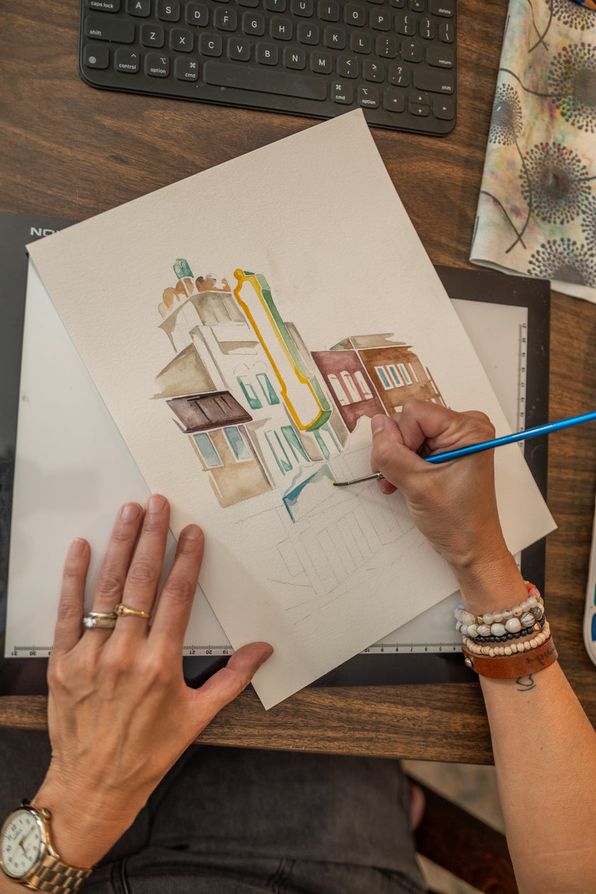 Watercolor painting in progress, showing Emily Frushour's hands as she creates an image of a theater in Michigan.