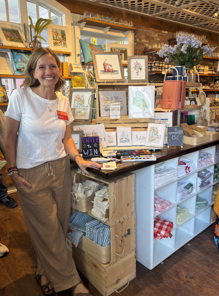 Artist Emily Frushour with artwork and watercolors at a store on Mackinac Island.