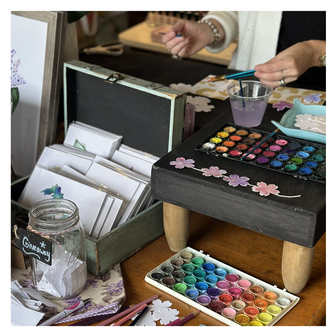 Watercolor supplies including paint, paintbrush, paper and flowers, on a table at a store.