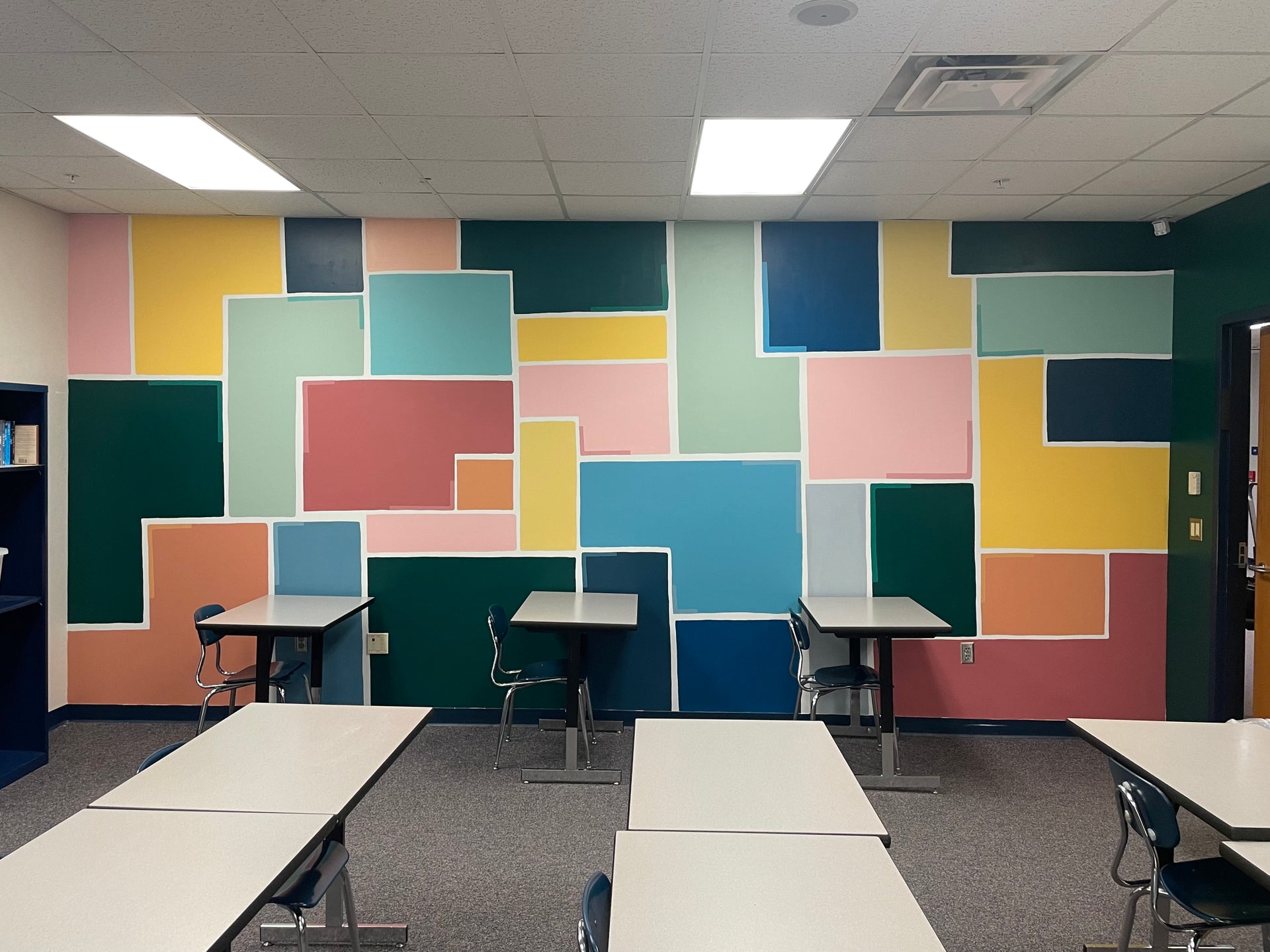 Bright and colorful geometric wall mural in a classroom with tables and chairs. Original artwork by artist Emily Frushour.