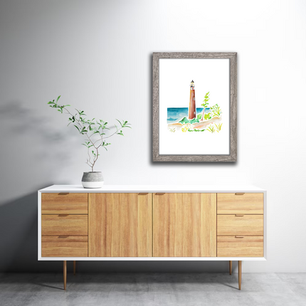 Gray frame wtih watercolor painting of Little Sable Point Lighthouse on Lake Michigan, surrounded by sand dunes and grass.