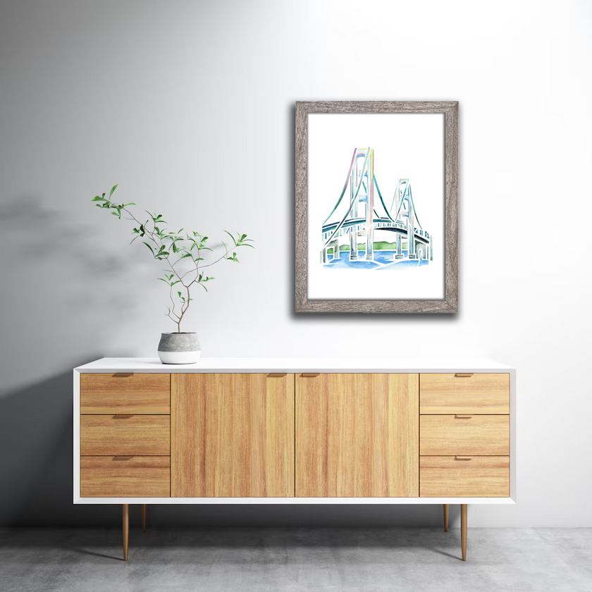 Watercolor painting of the Mackinac Bridge in Michigan, in soft pastel shades and clean lines. Art is hung on the wall in a gray frame.