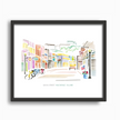 Fun and colorful watercolor scene from Main Street on Mackinac Island, with shops, bikes and a horse-drawn carriage. Original artwork by Emily Frushour, placed in a black frame.
