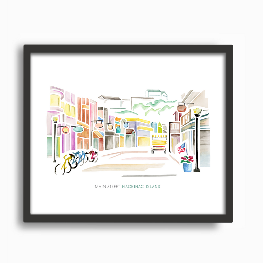 Fun and colorful watercolor scene from Main Street on Mackinac Island, with shops, bikes and a horse-drawn carriage. Original artwork by Emily Frushour, placed in a black frame.