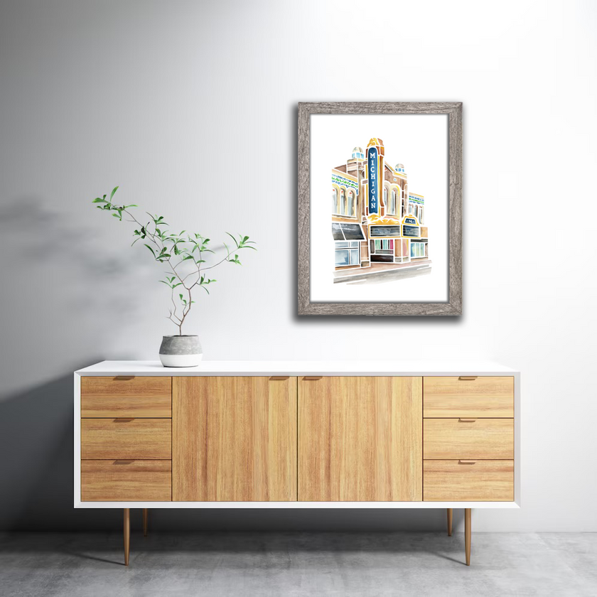 Colorful watercolor painting of he Michigan theater and marquee in Ann Arbor, Michigan. Shades of blue, brown, and gold. Framed in a gray frame.