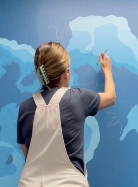 Artist Emily Frushour painting a large lake mural in shades of blue.