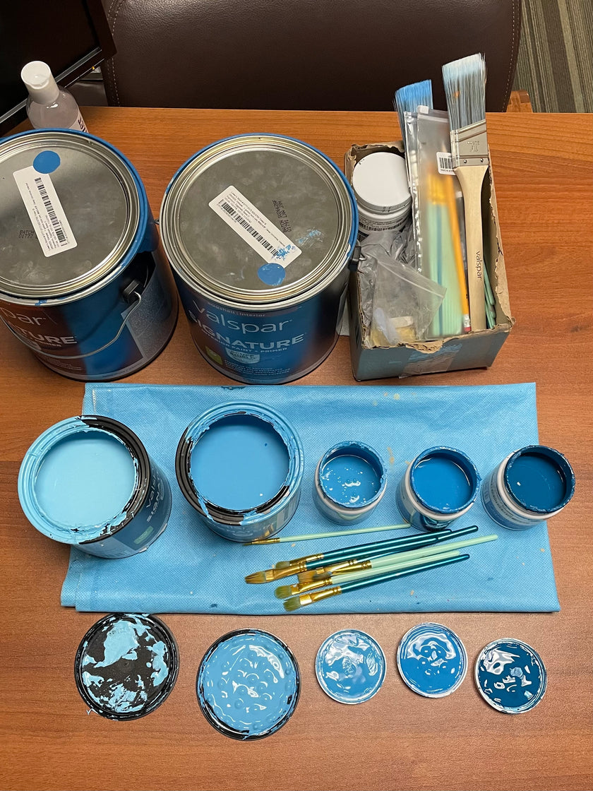 Painting supplies for creating a mural. Various blue paints and paintbrushes on a dropcloth.