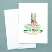 Folded white notecard with watercolor painting of Beaumont Tower in East Lansing, a brick tower surrounded by trees and landscaping, with envelope.
