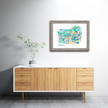 Colorful watercolor painting of a map of Petoskey, Michigan, in a gray frame hanging on a wall.