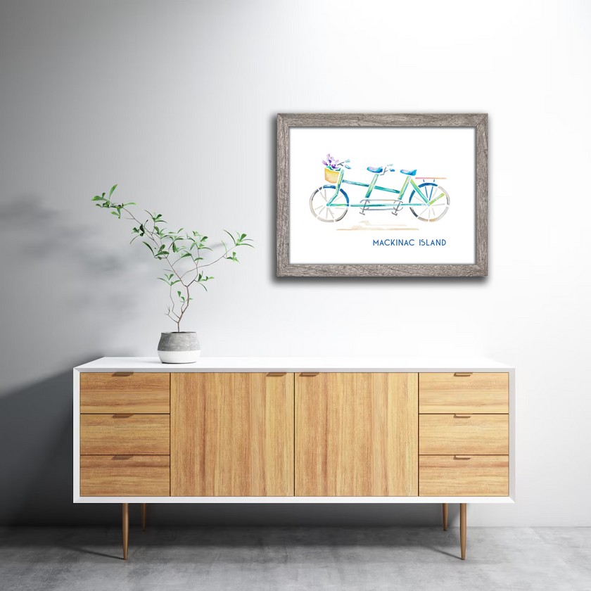 Colorful watercolor print of a green and blue tandem bike with the words Mackinac Island, in a gray frame in a home.
