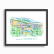 Bright and colorful watercolor painting showing a map of Traverse City, Michigan, in vibrant greens and blues, placed in a simple black frame.
