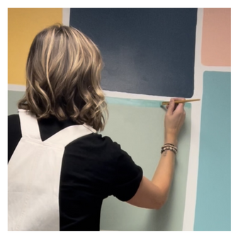 Close-up photo of an artist, Emily Frushour, painting a colorful classroom mural.