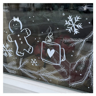 Delicate window art illustration for a cafe showing pine branches, hot cocoa, snowflakes and gingerbread man, created by artist Emily Frushour.
