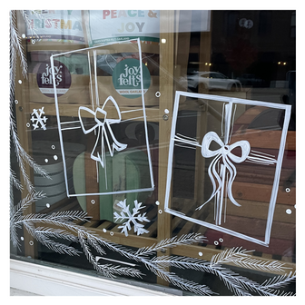 Delicate window art illustration showing pine branches and wrapped Christmas presents with snowflakes, created by artist Emily Frushour.