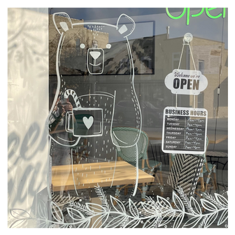 Delicate window art illustration for coffee shop showing friendly bear drawing and hot cocoa, created by artist Emily Frushour.