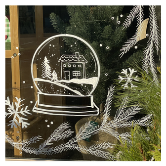 Delicate window art illustration showing pine branches and a snowglobe with a winter scene inside, created by artist Emily Frushour.